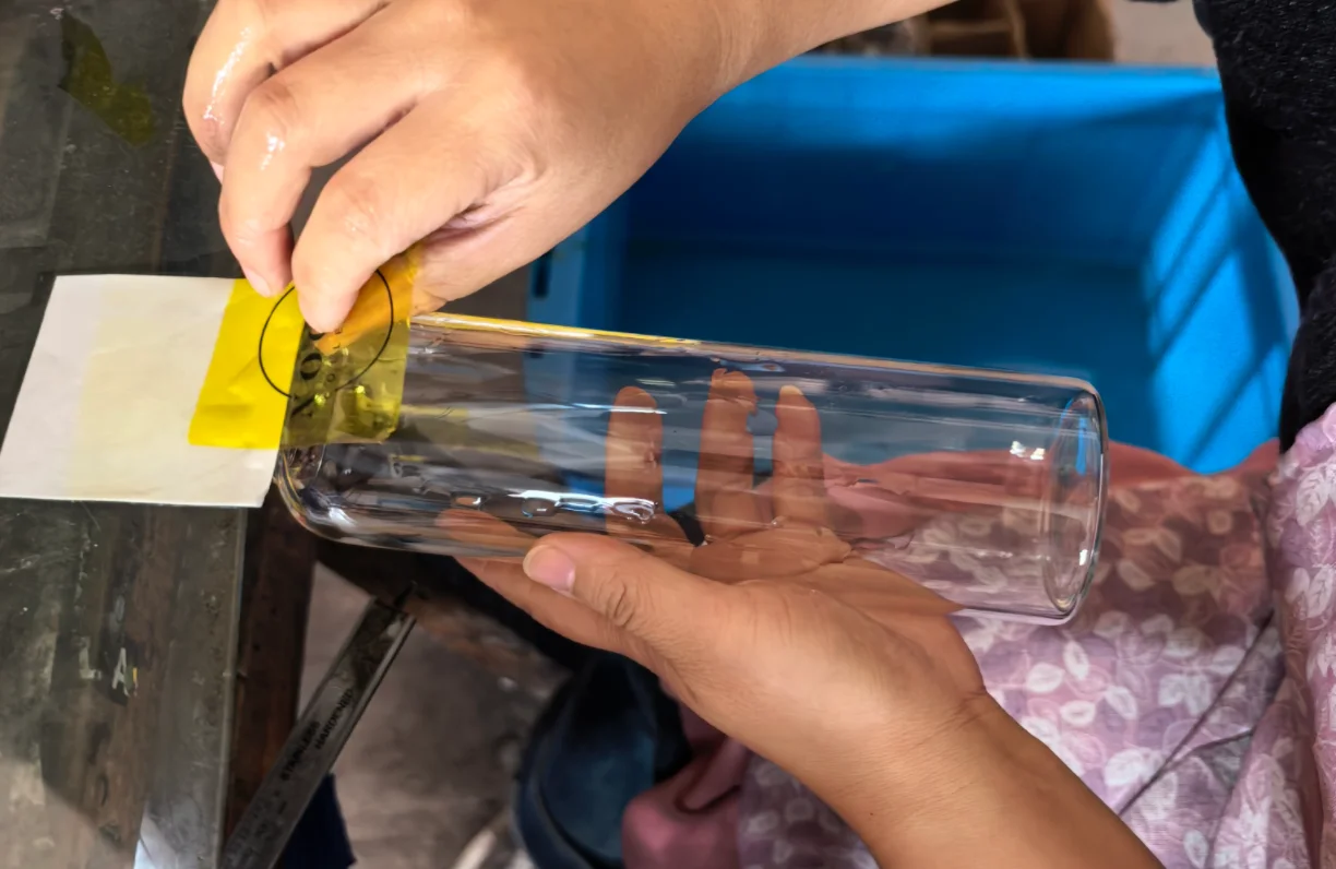 Person applying design template onto glass tumbler for customization process.
