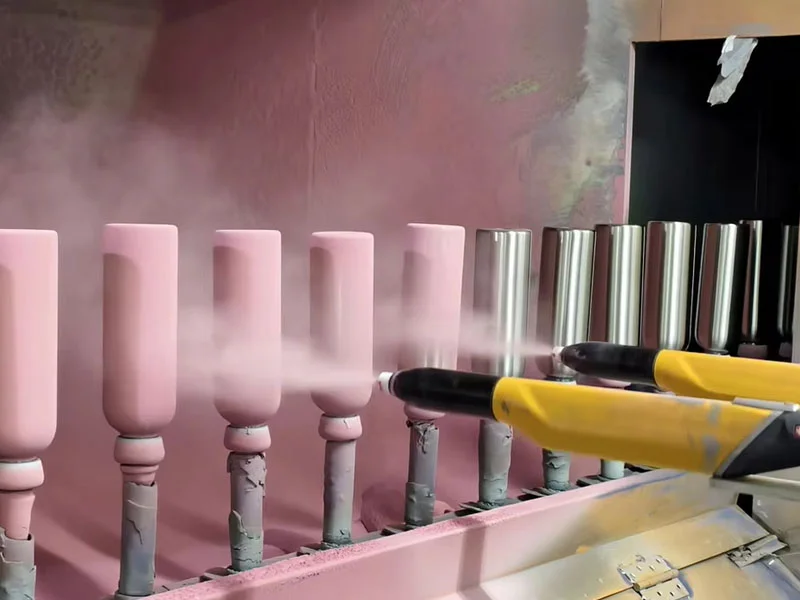 Industrial powder coating machines applying pink finish on stainless steel mugs during production.