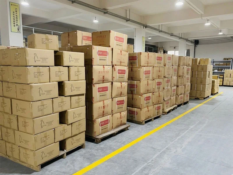 Stacks of cardboard boxes on pallets in a spacious warehouse with bright lighting.