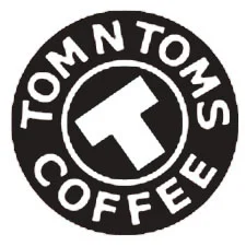 Black and white circular logo of Tom N Toms Coffee featuring a prominent 'T' surrounded by text.