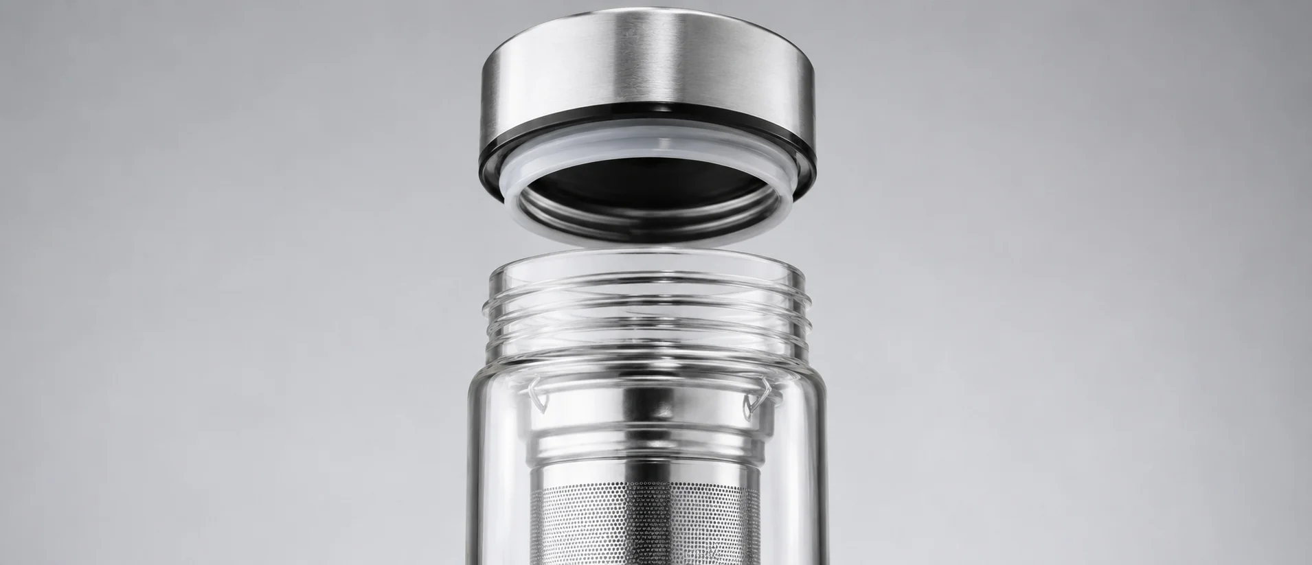 Close-up of a glass bottle with a detachable stainless steel lid and built-in tea infuser on a grey background.