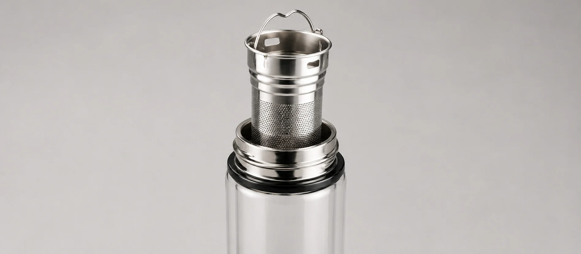 Close-up of a stainless steel tea infuser in a bottle with a metal mesh filter and handle on a gray background.